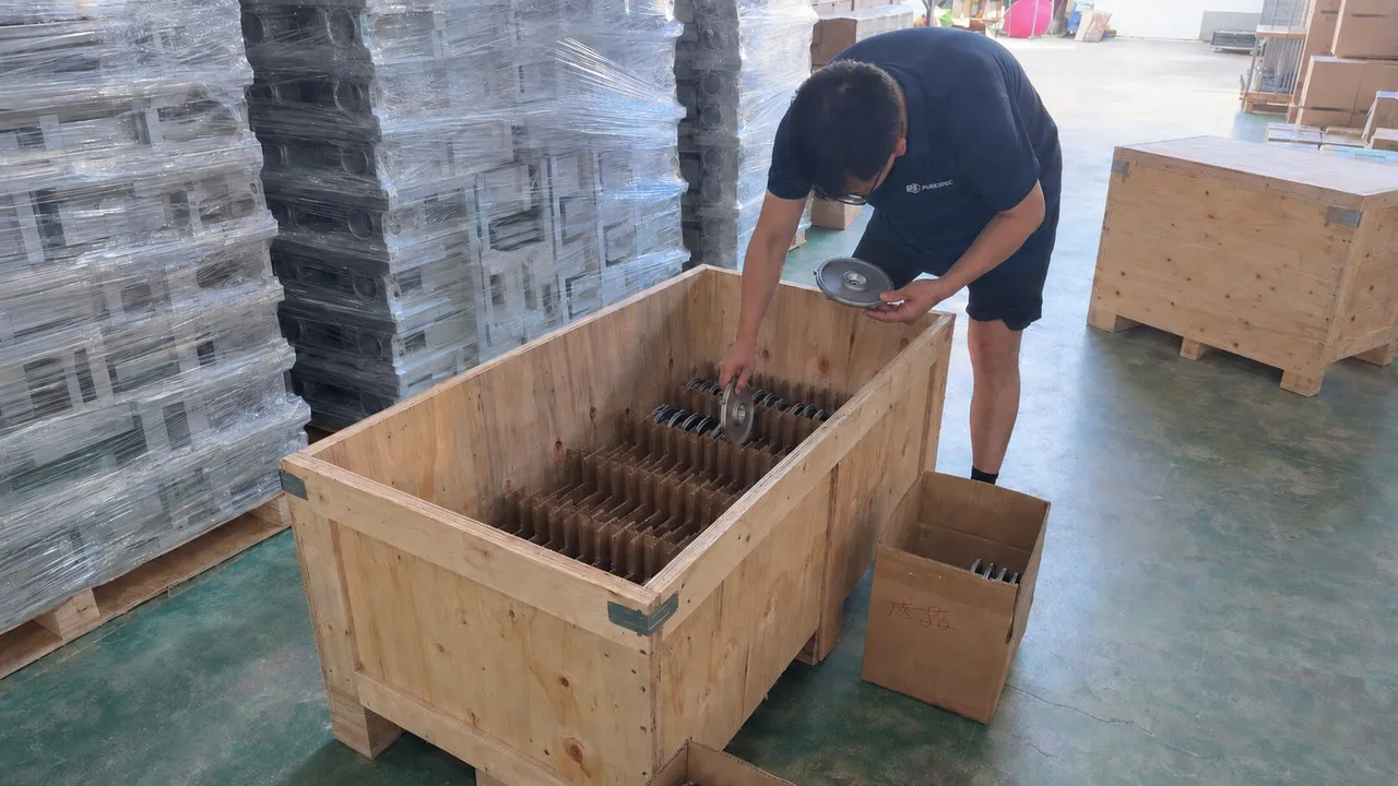 Worker packing finished metal parts into a wooden export crate for shipment.