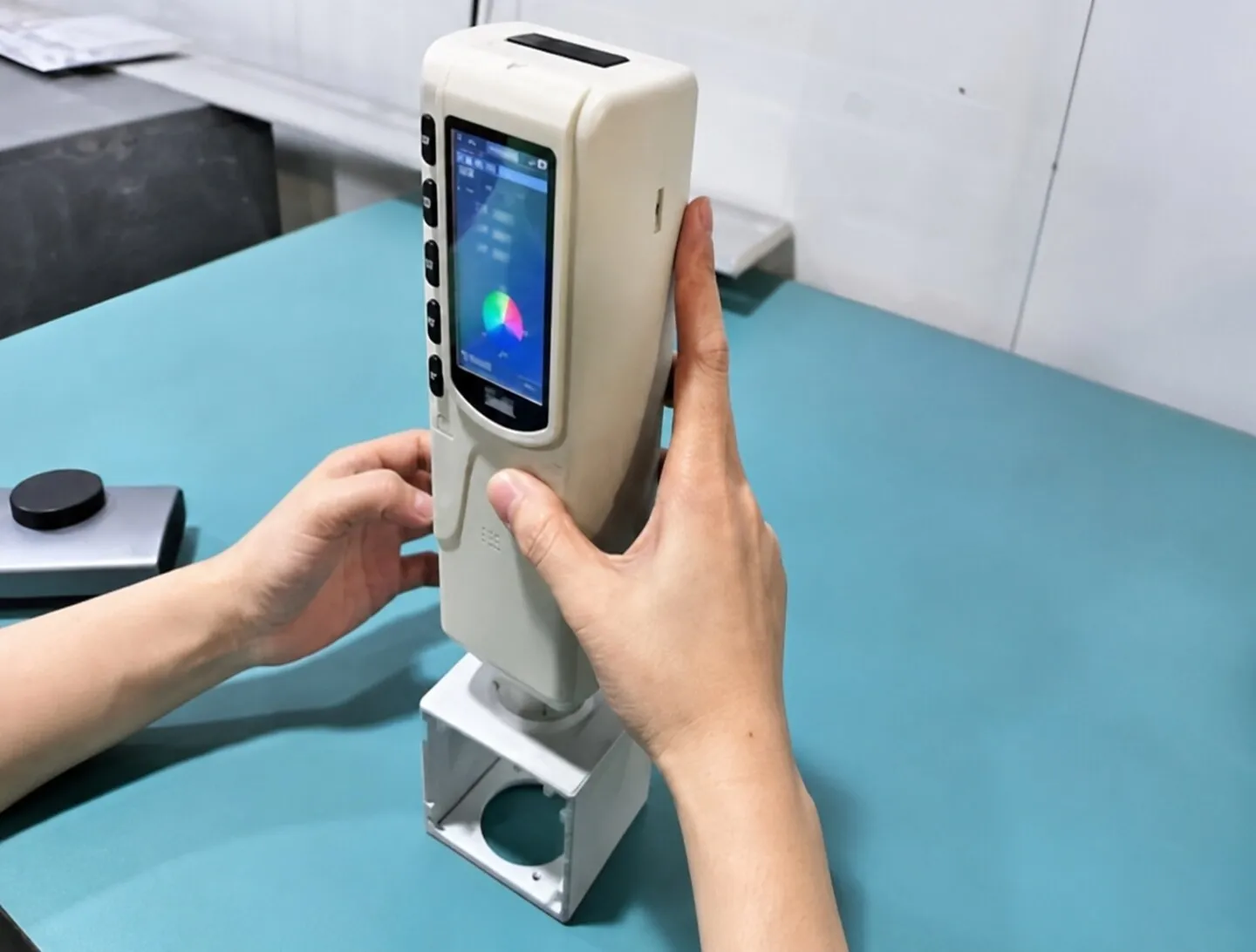 Handheld colorimeter measuring the finish color of a white sheet metal bracket.