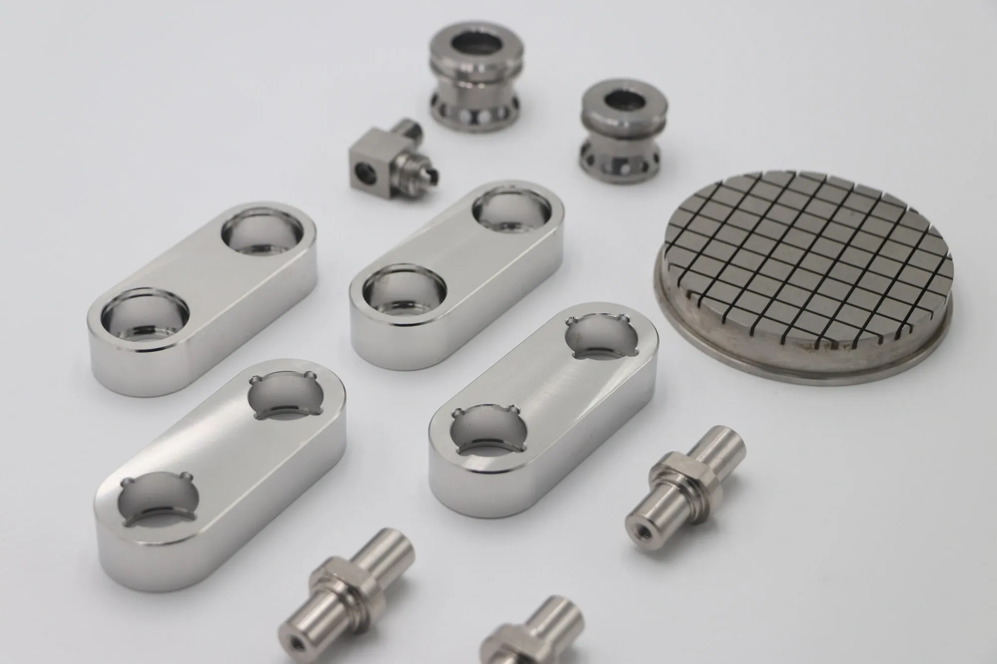 Mirror-polished machined stainless steel components including link blocks, turned fittings and a cross-grooved disc