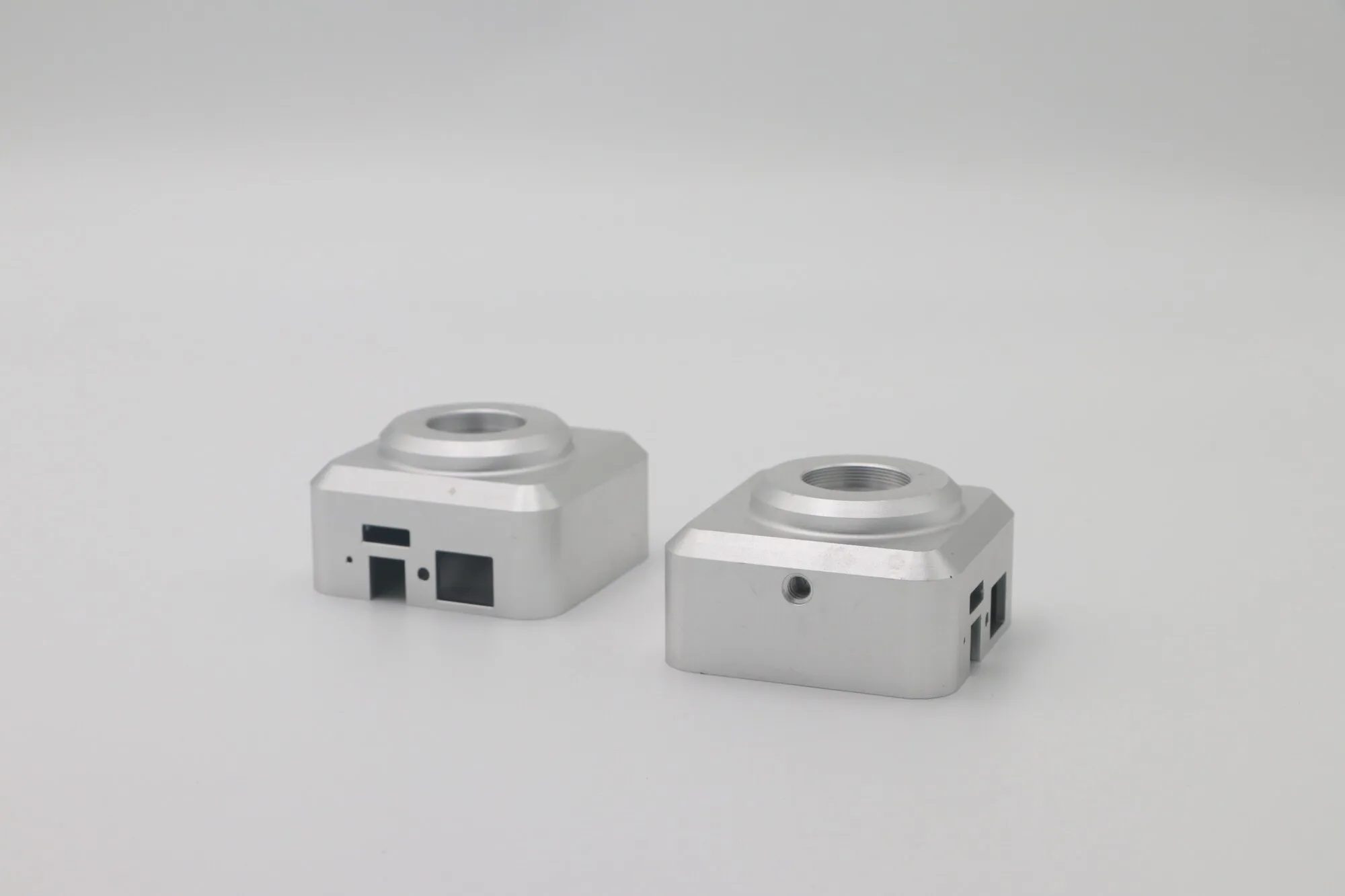 Pair of small machined aluminum sensor housings with raised bosses and cable apertures