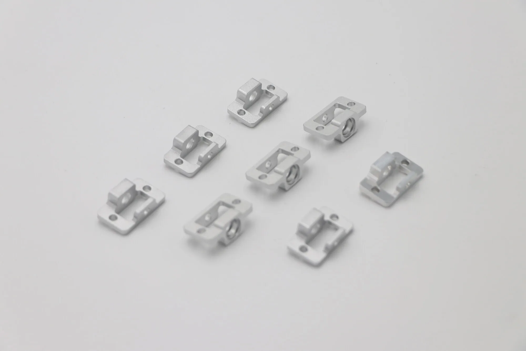 Batch of eight identical small CNC milled aluminum clamp blocks with bead blasted finish